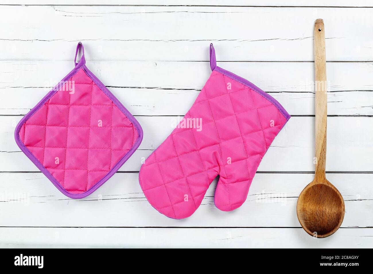 guanto da cucina, porta pentole e mestolo in legno su tavole di legno bianche Foto Stock