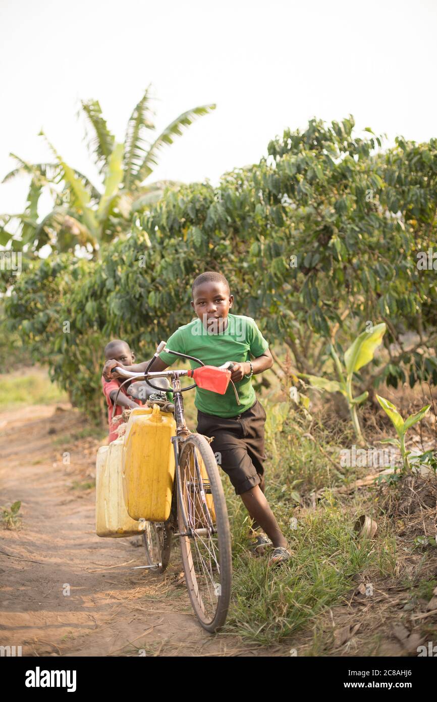 I bambini usano una bicicletta per prendere e trasportare acqua in un villaggio rurale nel distretto di Rakai, Uganda, Africa orientale. Foto Stock