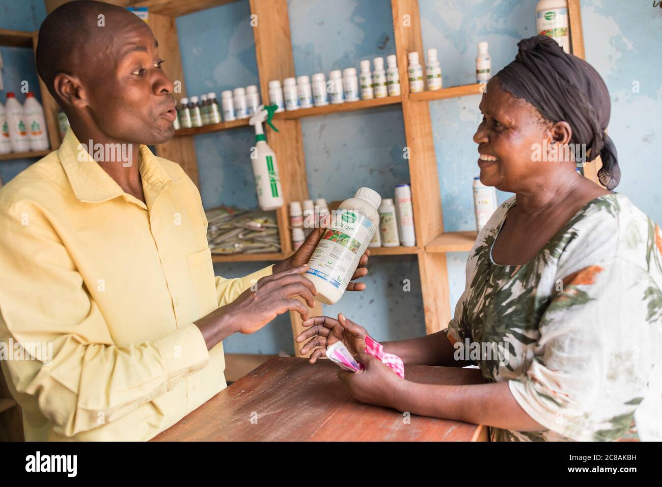 Un piccolo negozio di forniture agricole vende prodotti agricoli ad una cliente donna nel distretto di Kyotera, Uganda, Africa orientale. Foto Stock