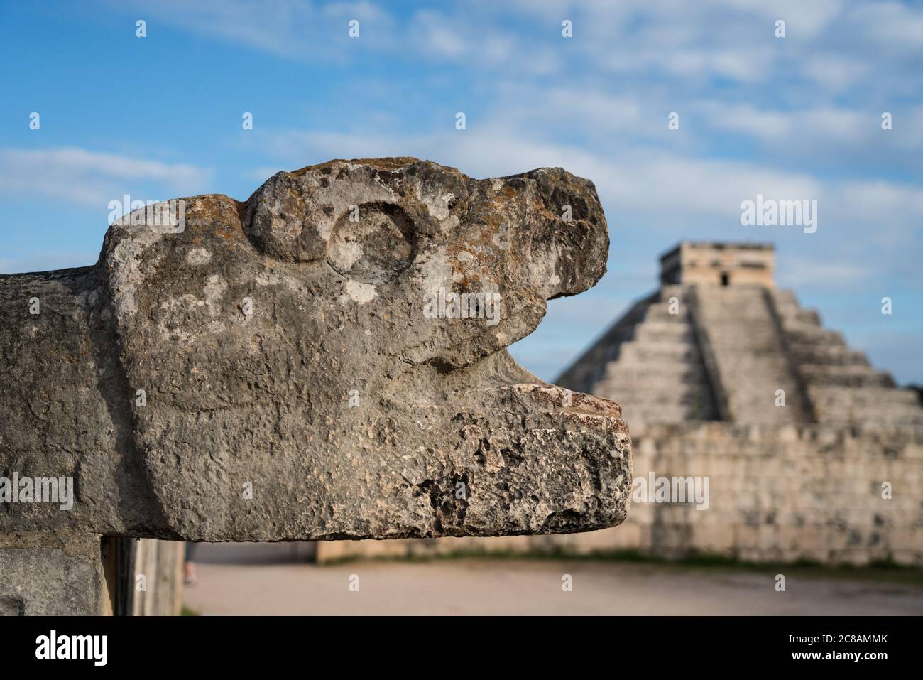 Una testa di pietra scolpita giaguaro al campo da ballo grande nelle rovine della città maya di Chichen Itza, Yucatan, Messico. Dietro c'è il Grande Pirami Foto Stock