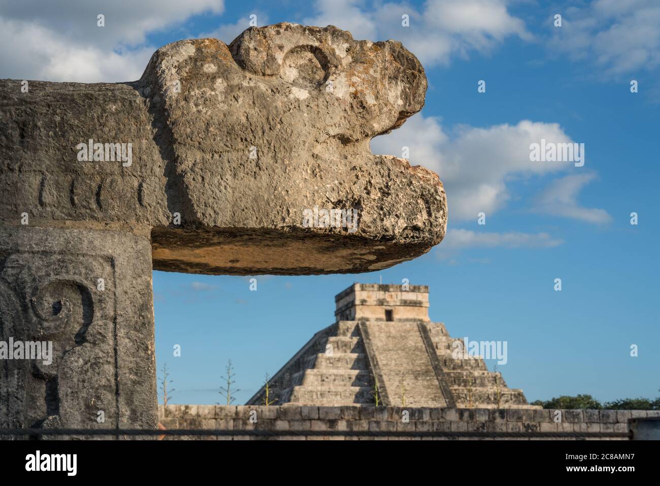 Una testa di pietra scolpita giaguaro al campo da ballo grande nelle rovine della città maya di Chichen Itza, Yucatan, Messico. Dietro c'è il Grande Pirami Foto Stock