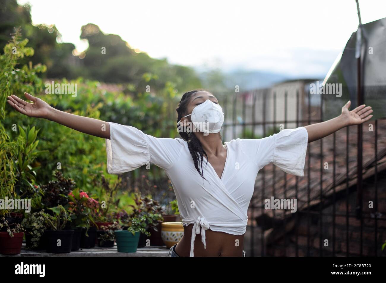 Giovane donna nera in maschera facciale apre le braccia e si rilassa in balcone Foto Stock