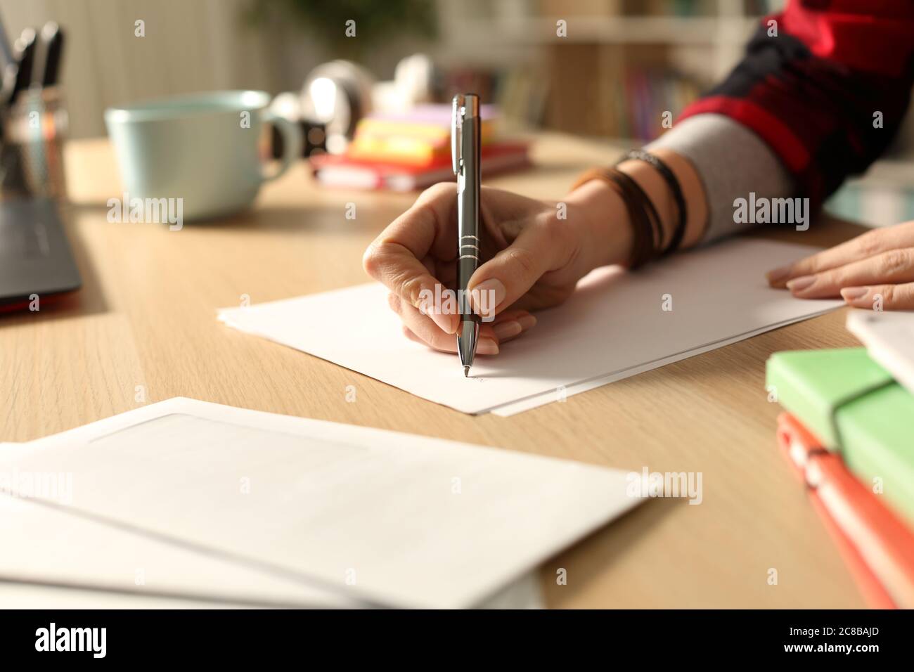 Primo piano della lettera scritta da una mano di studente su una scrivania a casa di notte Foto Stock