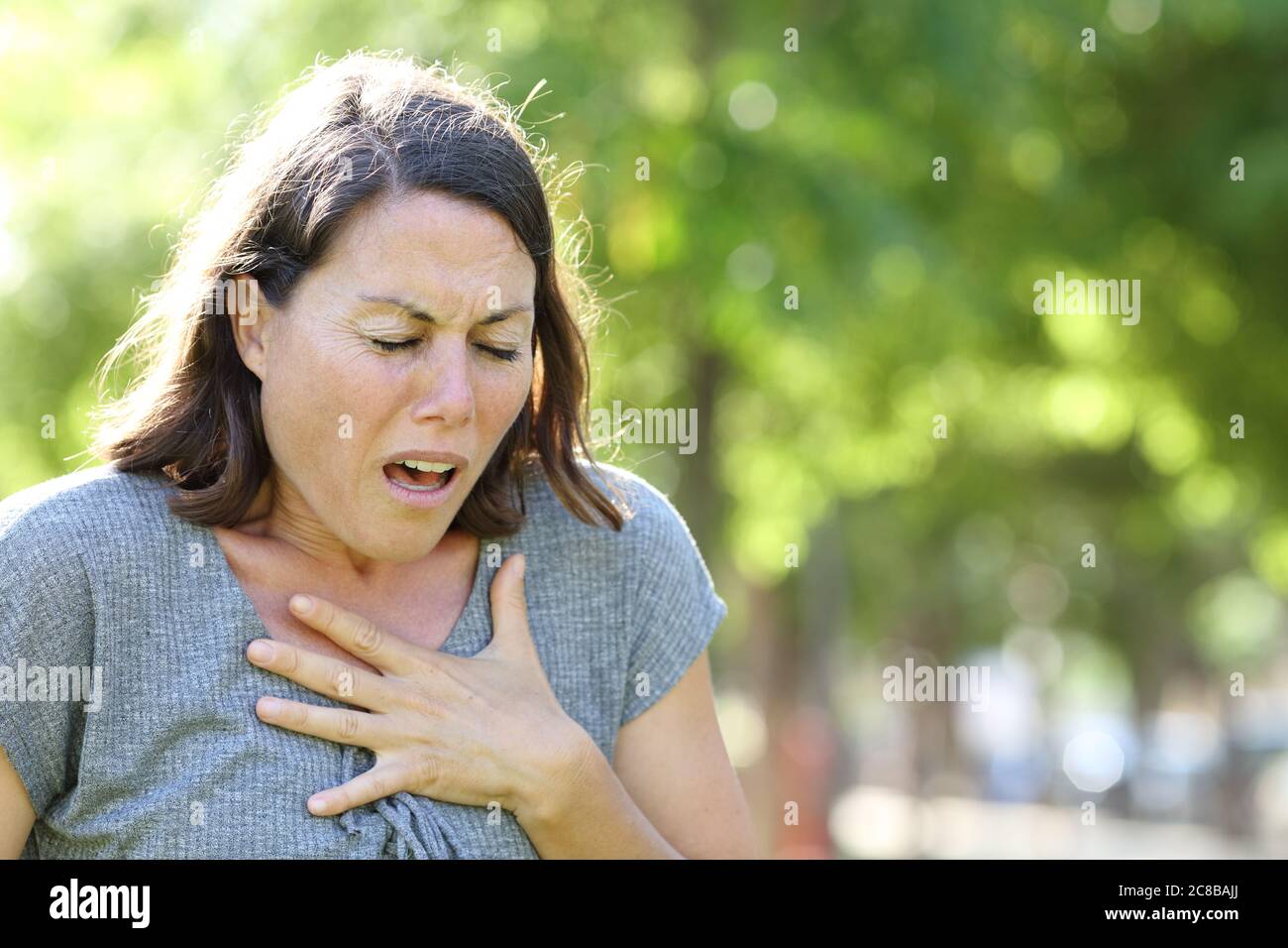 Donna di mezza età sibilante che tiene il petto in piedi in un parco in estate Foto Stock