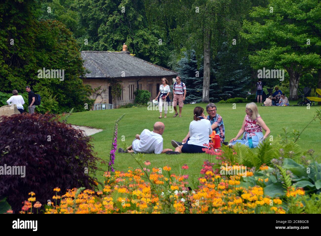 Due coppie sab sul prato che ha un picnic al RHS Garden Harlow Carr, Harrogate, Yorkshire, Inghilterra, UK. Foto Stock