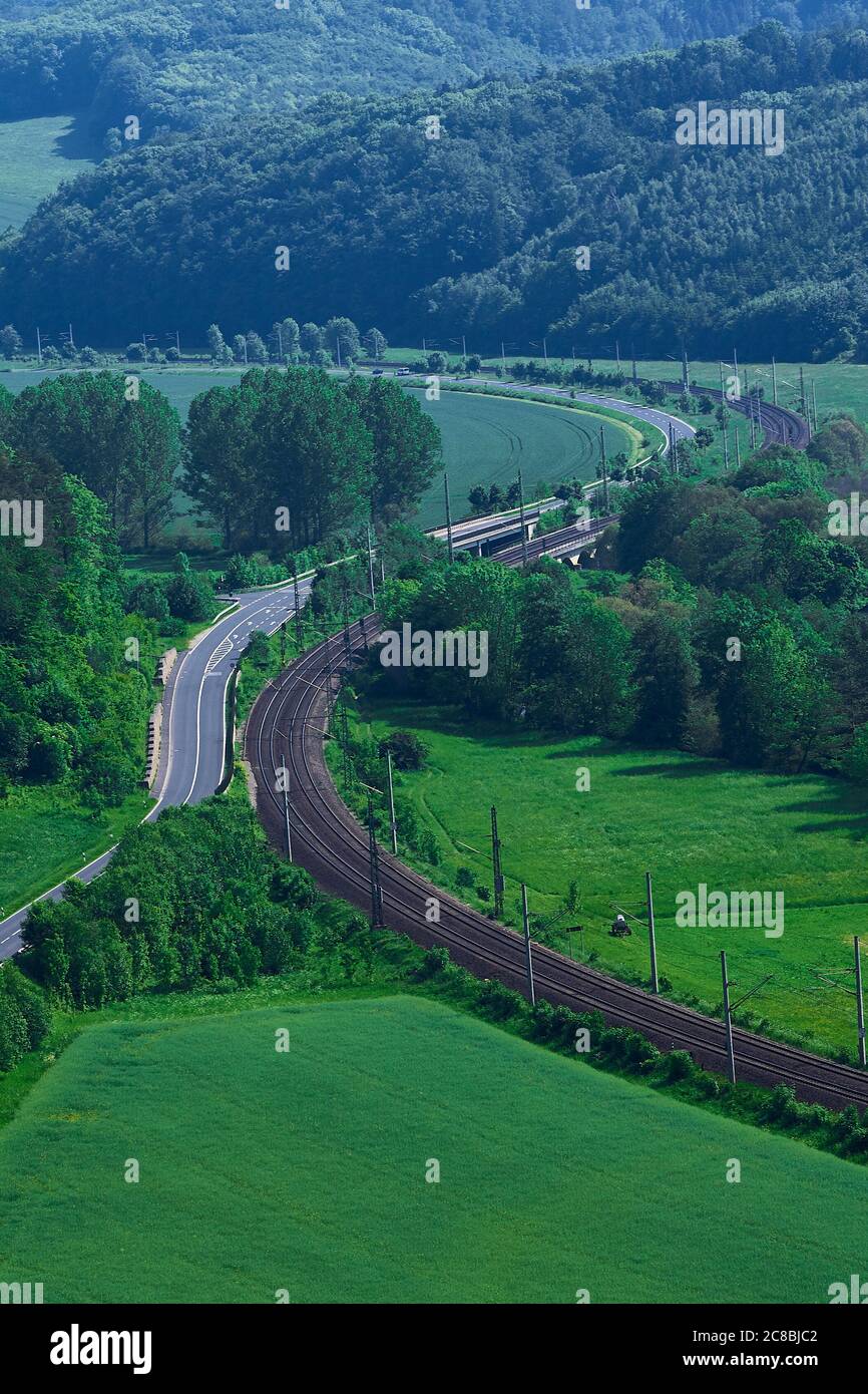 Binari ferroviari lungo lato di una strada asfaltata attraverso la foresta. Foto Stock