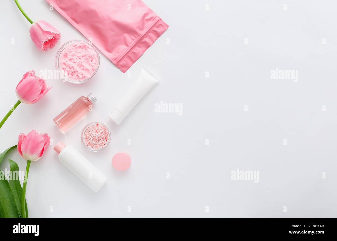 Prodotti rosa per bagno di cura della pelle. Bottiglie cosmetiche, provette, confezionamento in crema, polvere e perle per vasche da bagno con rosa. Centro benessere cosmetico Foto Stock