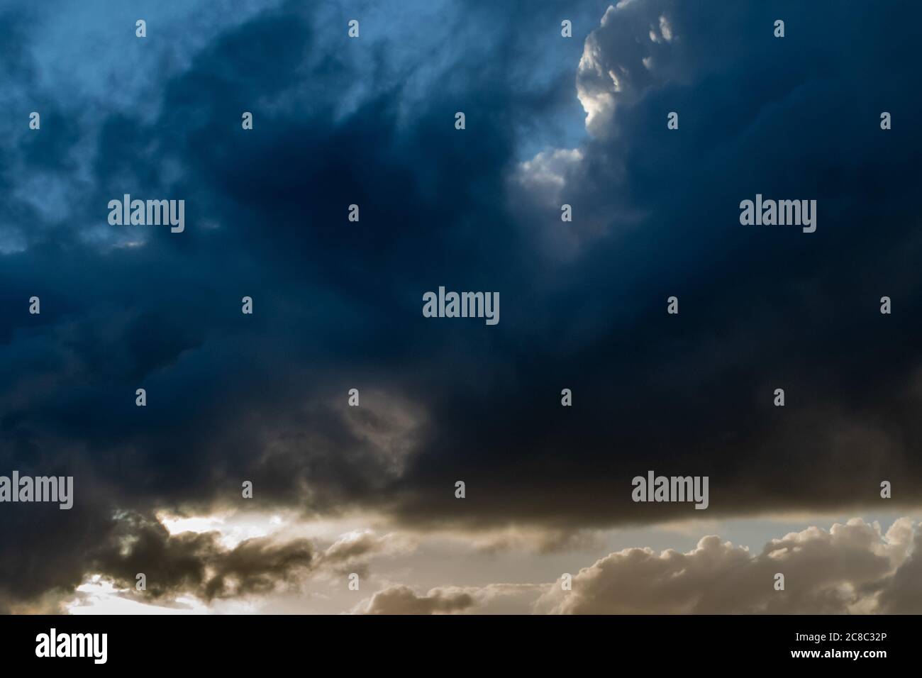 Nuvole scure e tempestose si avvolgerono attraverso il cielo con luce bianca brillante che si luce sul fondo Foto Stock