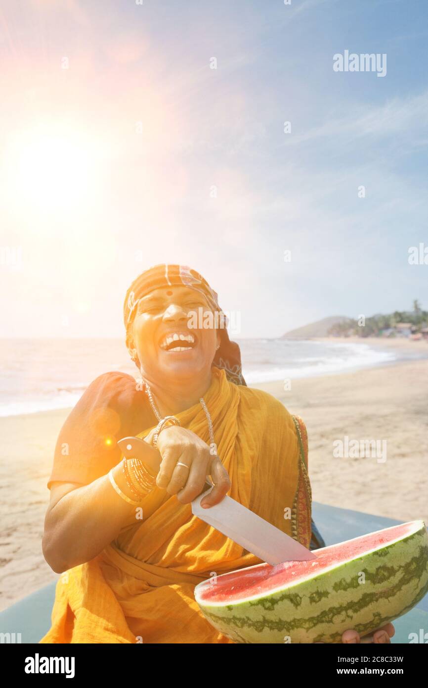 Felice matura indiana donna taglio anguria a Vagator Beach Foto Stock
