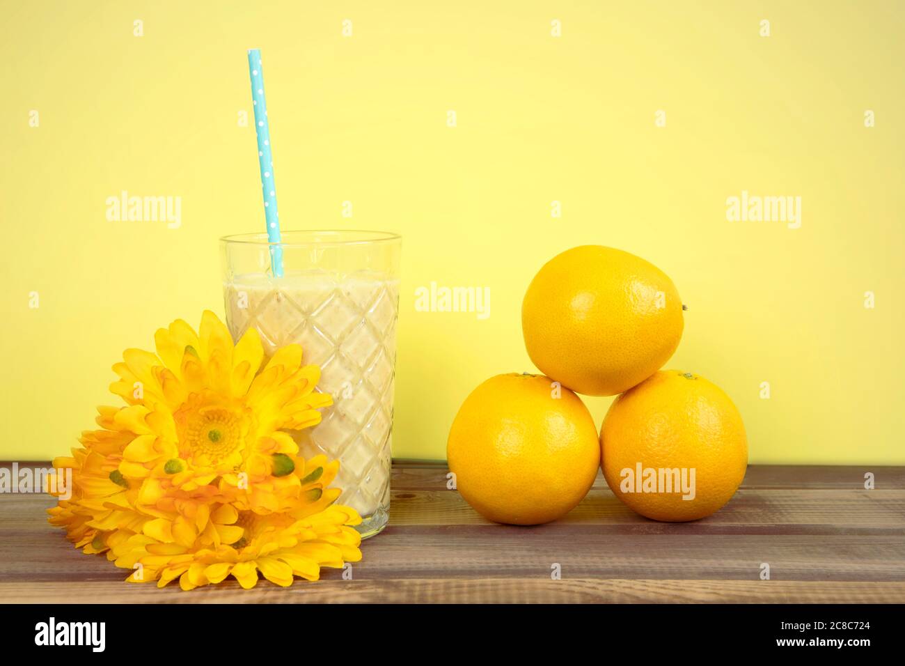Cocktail di frutta in stile retrò in estate. Frullato giallo in vetro con disposizione di paglia, frutta arancio e fiori. Foto Stock