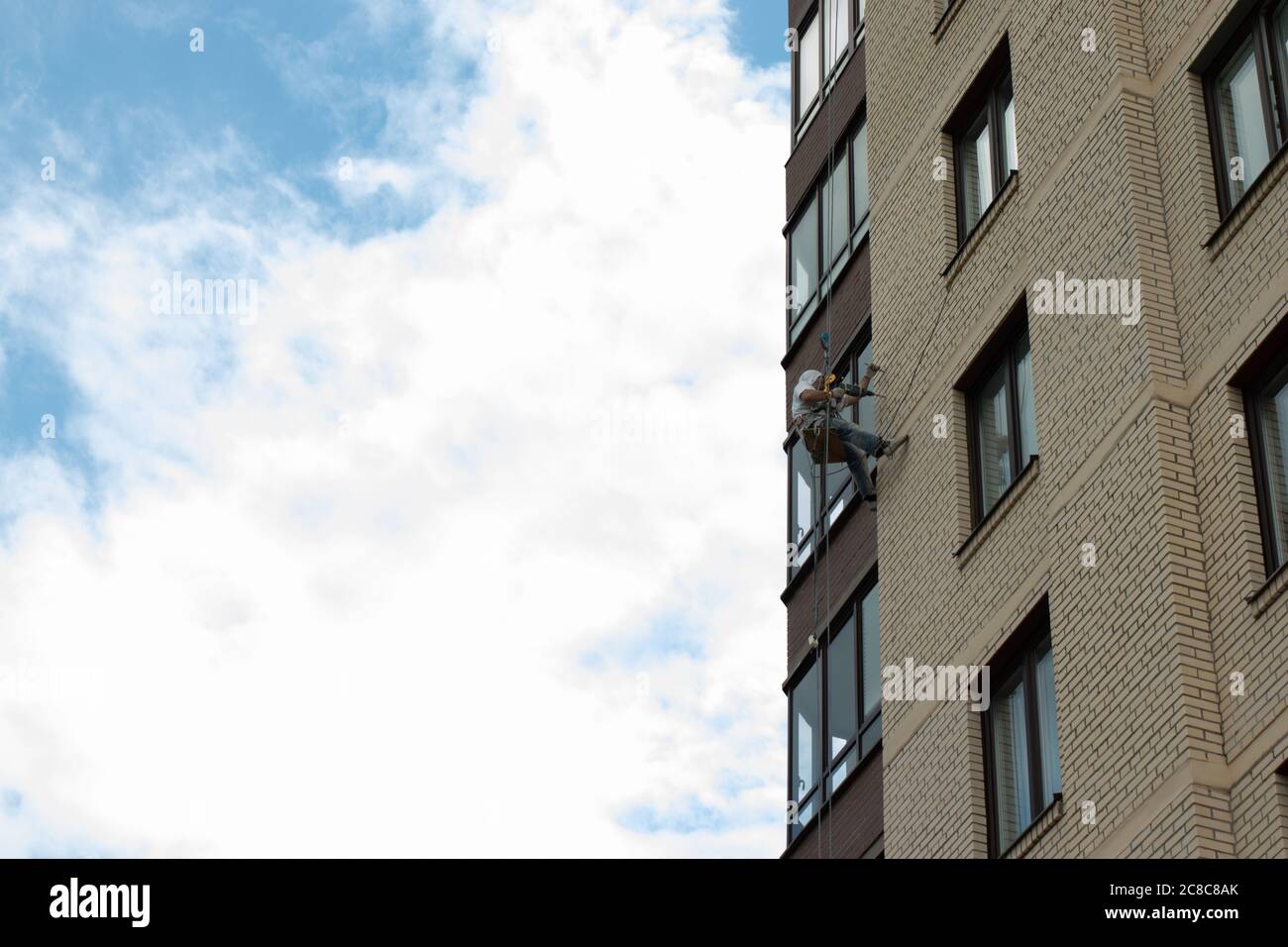 Un lavoratore pende su una corda su un edificio. Lavorare in altezza. Lavaggio e decorazione domestica. Spazio di copia Foto Stock