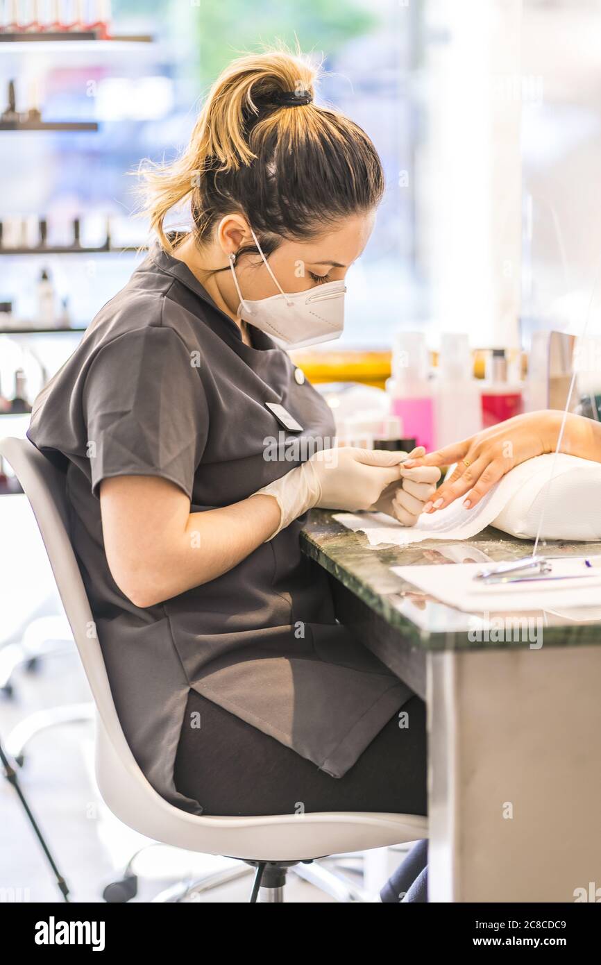 Shallow focus immagine verticale di un'artista di unghie ispanica femminile che indossa maschera pittura unghie del cliente Foto Stock