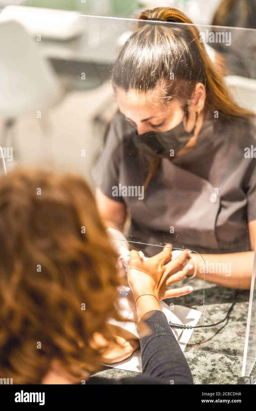 Shallow focus immagine verticale di un'artista di unghie ispanica femminile che indossa maschera pittura unghie del cliente Foto Stock