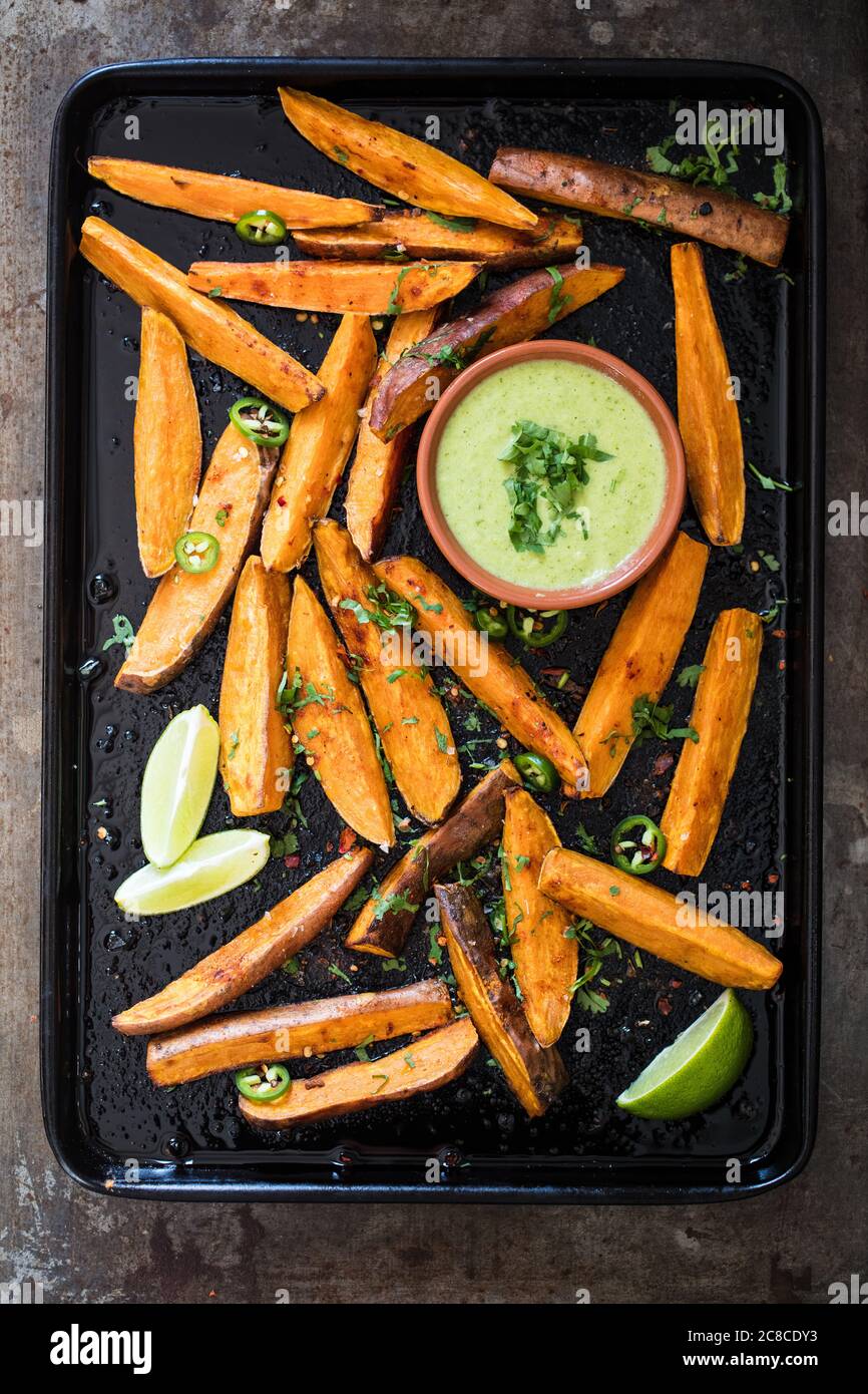 Spicchi di patate dolci con spezie cajun, salsa di coriandolo e spicchi di lime Foto Stock