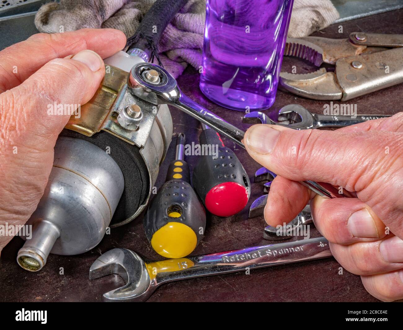 Chiusura delle mani di un uomo che tiene la pompa carburante di un veicolo su un banco di lavoro ordinato, allentando o serrando i dadi delle staffe con una chiave a cricchetto. Foto Stock