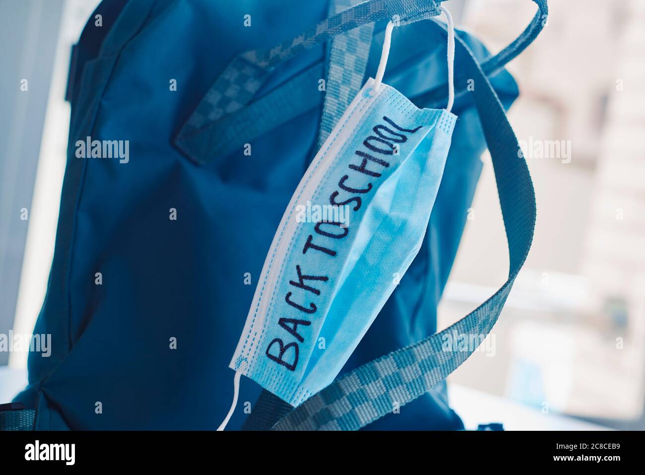 chiusura di un bookbag verde e di una maschera chirurgica blu con il testo di ritorno a scuola scritto in esso, che raffigura la necessità di prevenire l'infezione a scuola Foto Stock