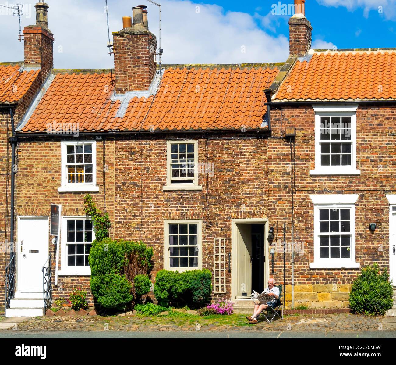 Un anziano gentiluomo seduto a leggere il suo giornale fuori del suo cottage terrazzato accanto al fiume Leven nel centro di Stokesley North Yorkshire Foto Stock