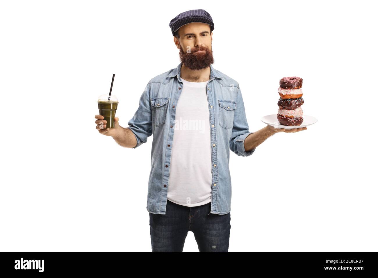 Uomo bearded che tiene un frullato verde e un piatto di ciambelle di cioccolato, cibo sano contro malsano, isolato su sfondo bianco Foto Stock