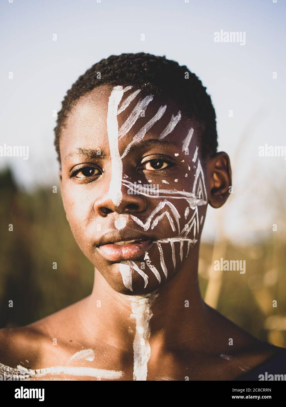 ritratto di un ragazzo africano con pittura etnica del viso e vestirsi nel cespuglio Foto Stock