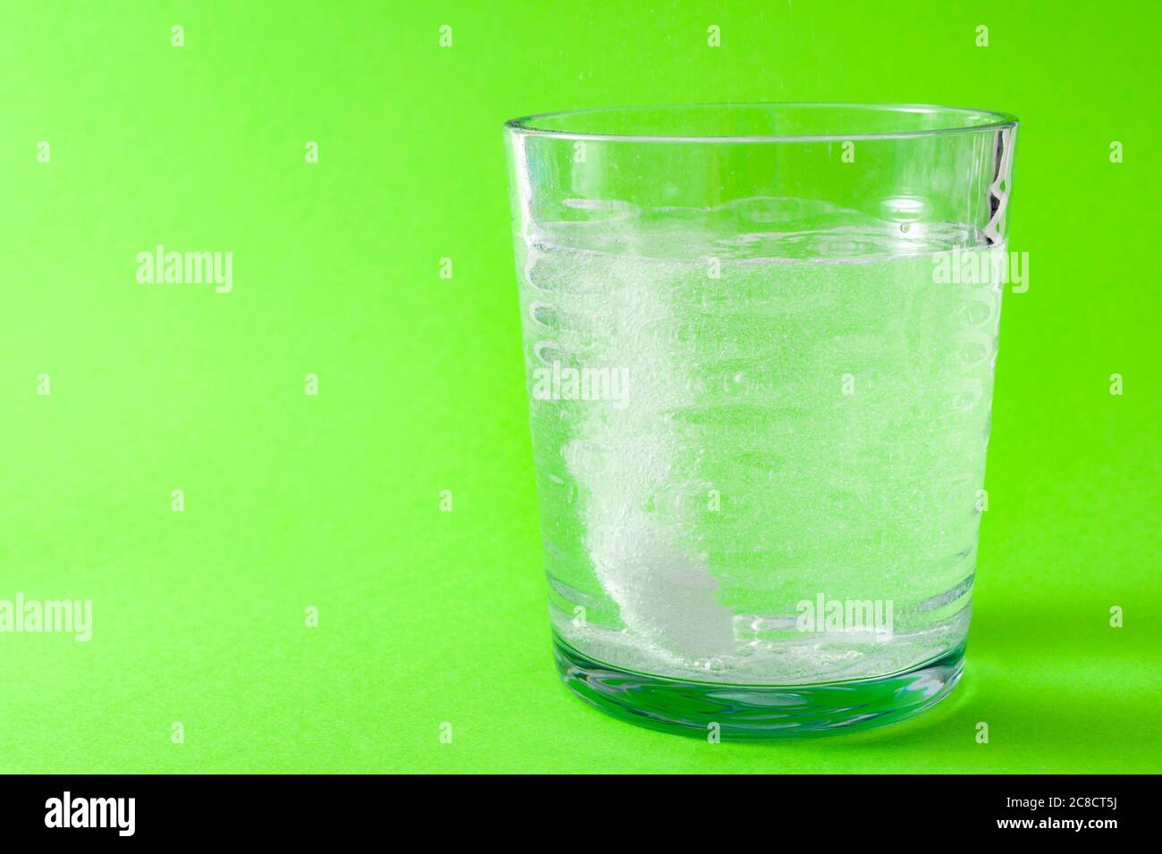 Trattamento del freddo e dell'influenza e concetto di medicina del mal di testa con un aspirina effervescente gocciolato in un bicchiere d'acqua circondato da bolle frizzanti isolato su g. Foto Stock