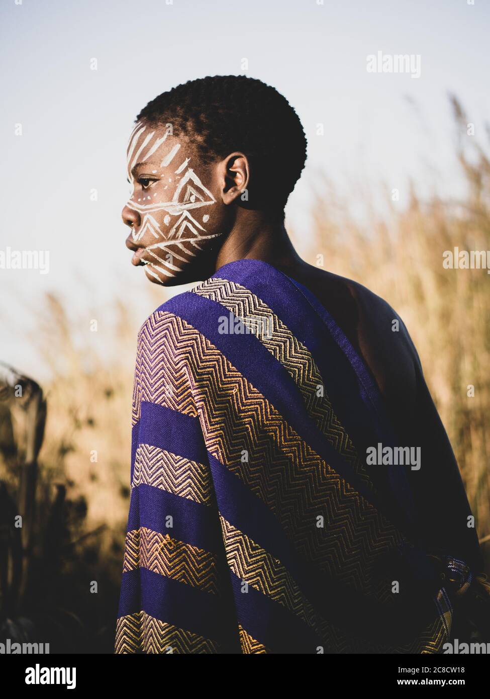 ritratto di un ragazzo africano con pittura etnica del viso e vestirsi nel cespuglio Foto Stock