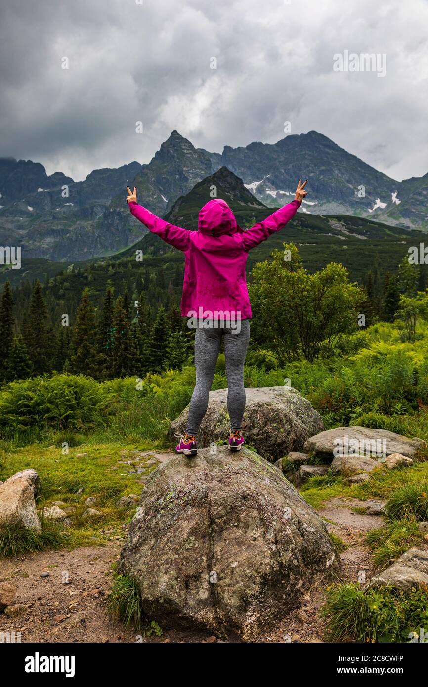 Donna con cappuccio che guarda il panorama del Tatra sotto la pioggia con le mani alte - orientamento ritratto Foto Stock