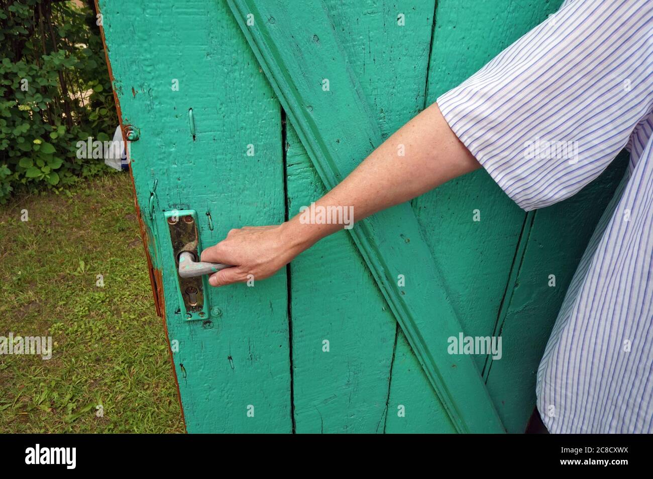 Donna matura villaggio apre una porta di legno al suo fienile Foto Stock