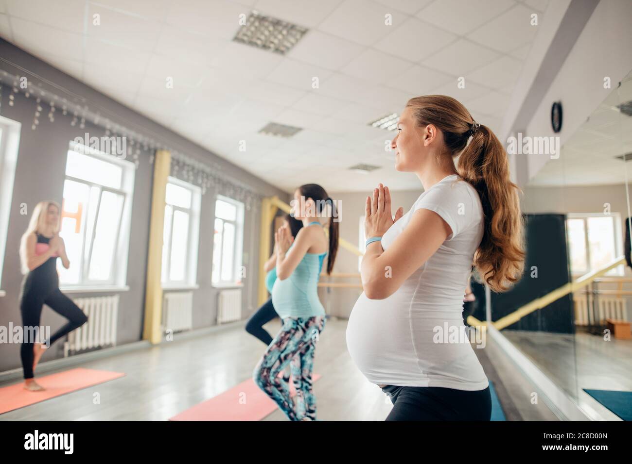Felici le donne in stato di gravidanza in corso di yoga in piedi in posizione dell'albero in un fitness studio Foto Stock