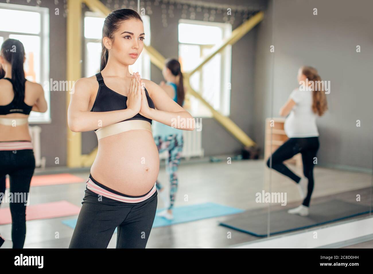 Felici le donne in stato di gravidanza in corso di yoga in piedi in posizione dell'albero in un fitness studio Foto Stock