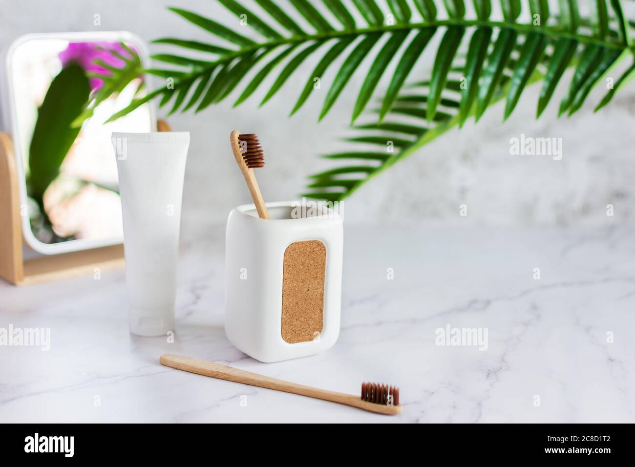 Spazzolini da denti in bambù in una tazza, dentifricio e specchio su un tavolo in marmo bianco in un bagno. Stile di vita sostenibile, concetto di igiene dentale. Foto Stock