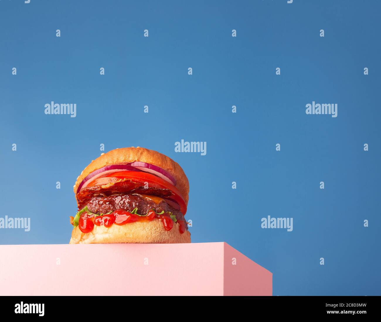 Hamburger di manzo fresco e succoso posto sul supporto e sfondo blu. Spazio di copia per testo, visualizzazione Hero alla moda, orizzontale Foto Stock