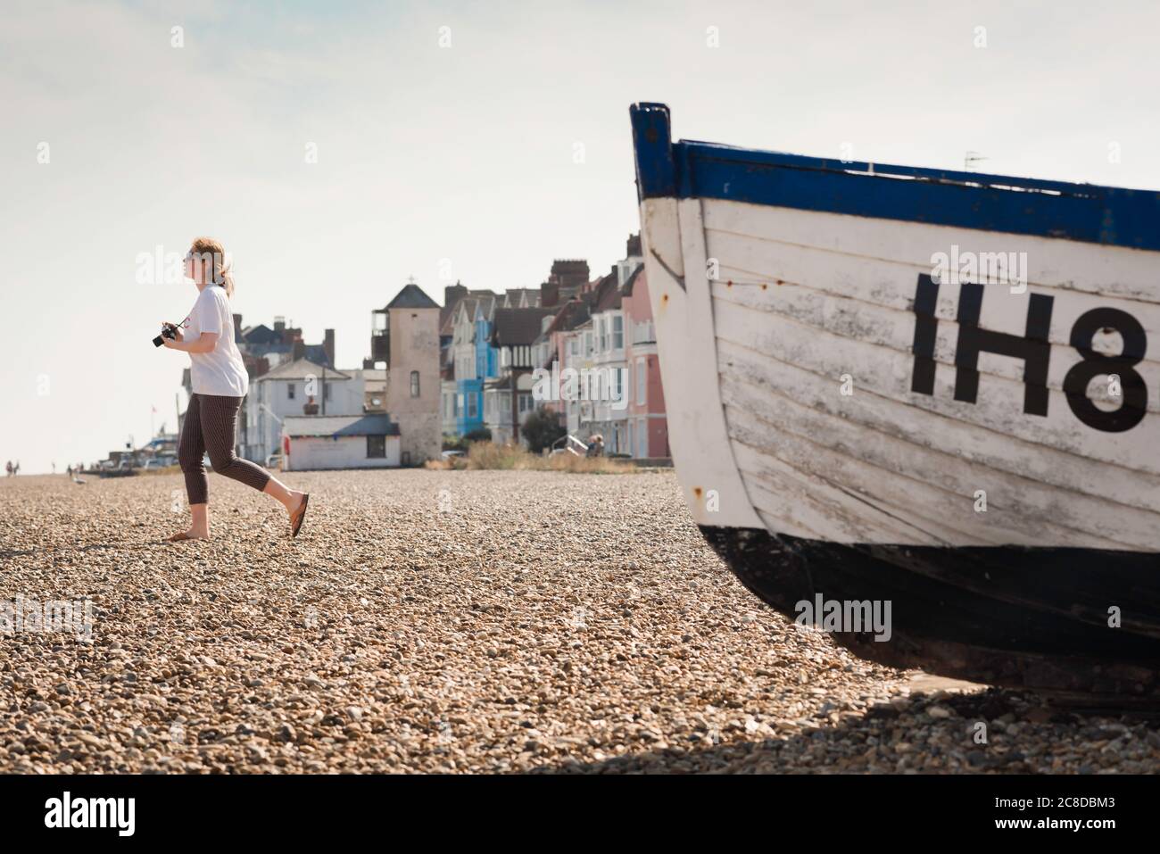 Fotografia di una giovane donna, vista di una giovane donna che tiene una macchina fotografica e cammina da sola su una spiaggia di Aldeburgh sulla costa del Suffolk, Inghilterra, Regno Unito Foto Stock