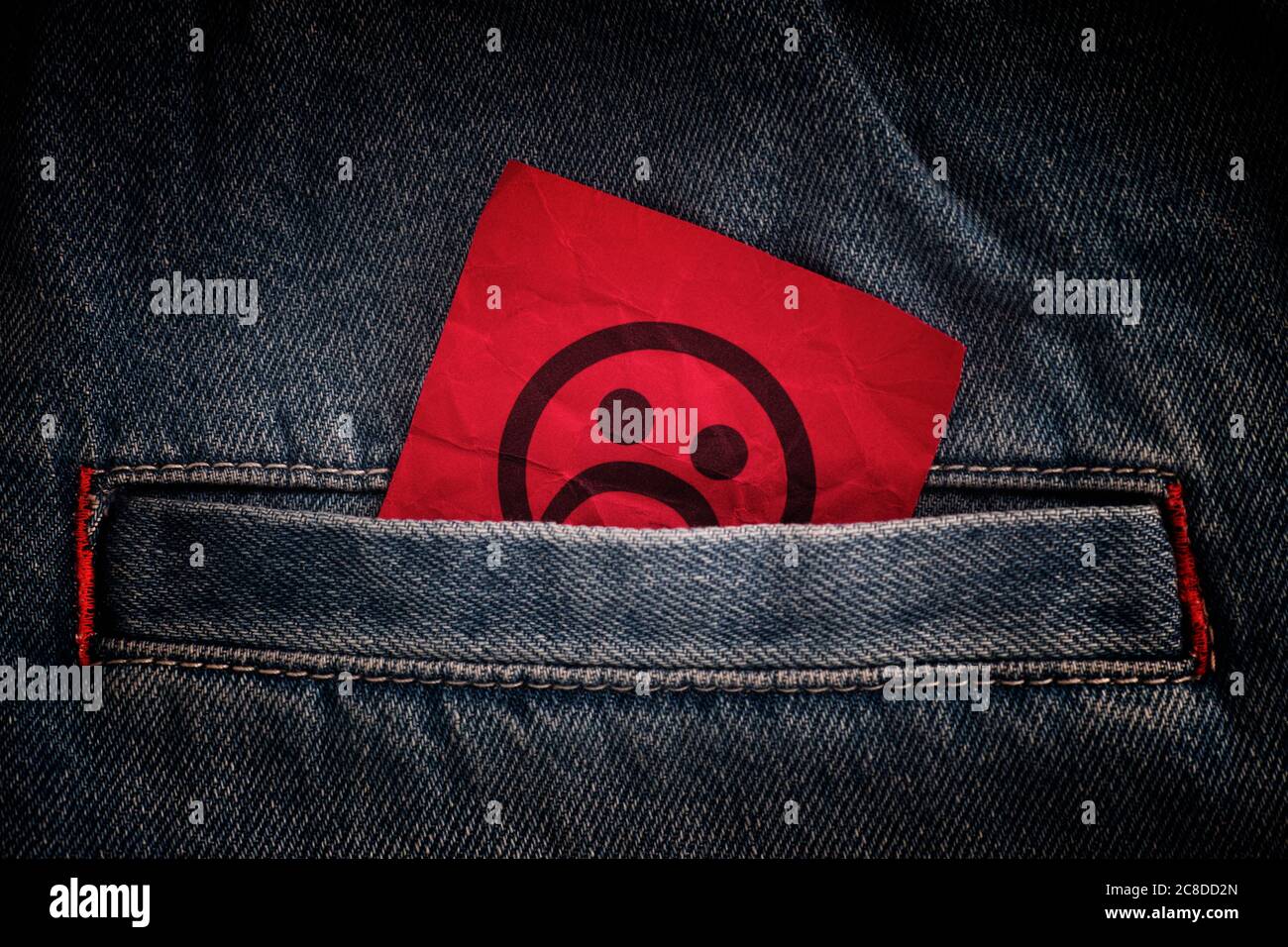 Una faccia triste che si stacca fuori da una tasca dei jeans. Primo piano. Foto Stock