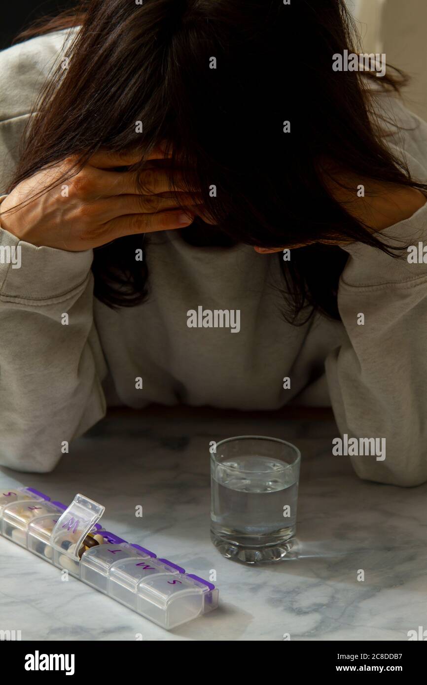 Una donna triste con la testa giù e le mani sulla sua testa è visto proprio prima che lei prende il suo farmaco quotidiano per la malattia cronica. Foto Stock