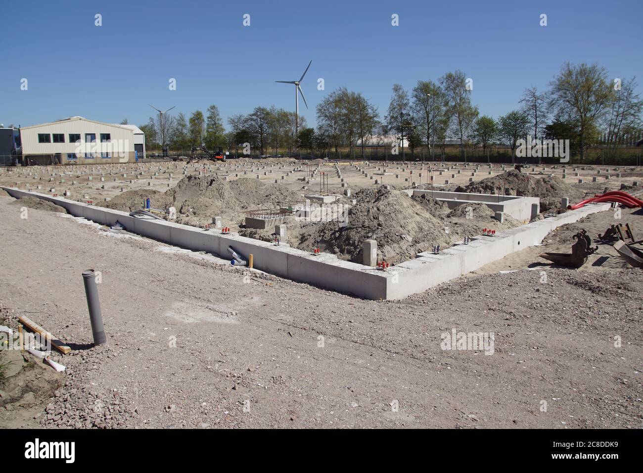 Pali di calcestruzzo prefabbricati quadrati in un luogo di costruzione. Condotto a suolo usando macchina di palo di calcestruzzo. In lontananza un moderno mulino a vento. Alkmaar. Olanda Foto Stock