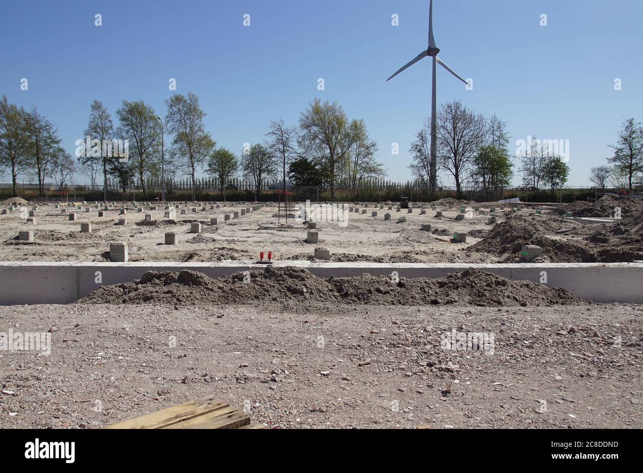 Pali di calcestruzzo prefabbricati quadrati in un luogo di costruzione. Condotto a suolo usando macchina di palo di calcestruzzo. In lontananza un moderno mulino a vento. Alkmaar. Olanda Foto Stock