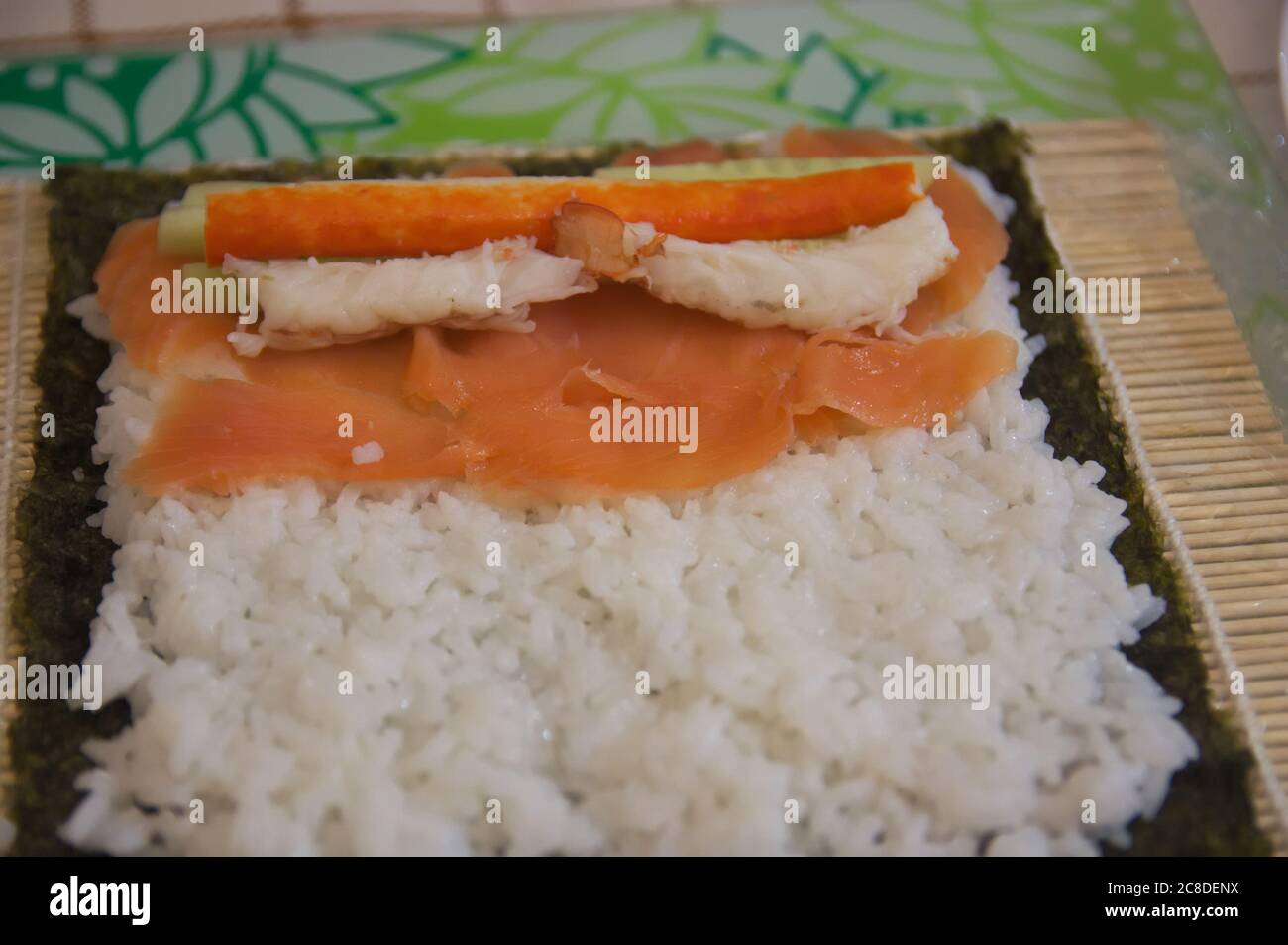 Primo piano di una tavola dove il sushi viene preparato con riso, pesce, verdure e alghe nori Foto Stock