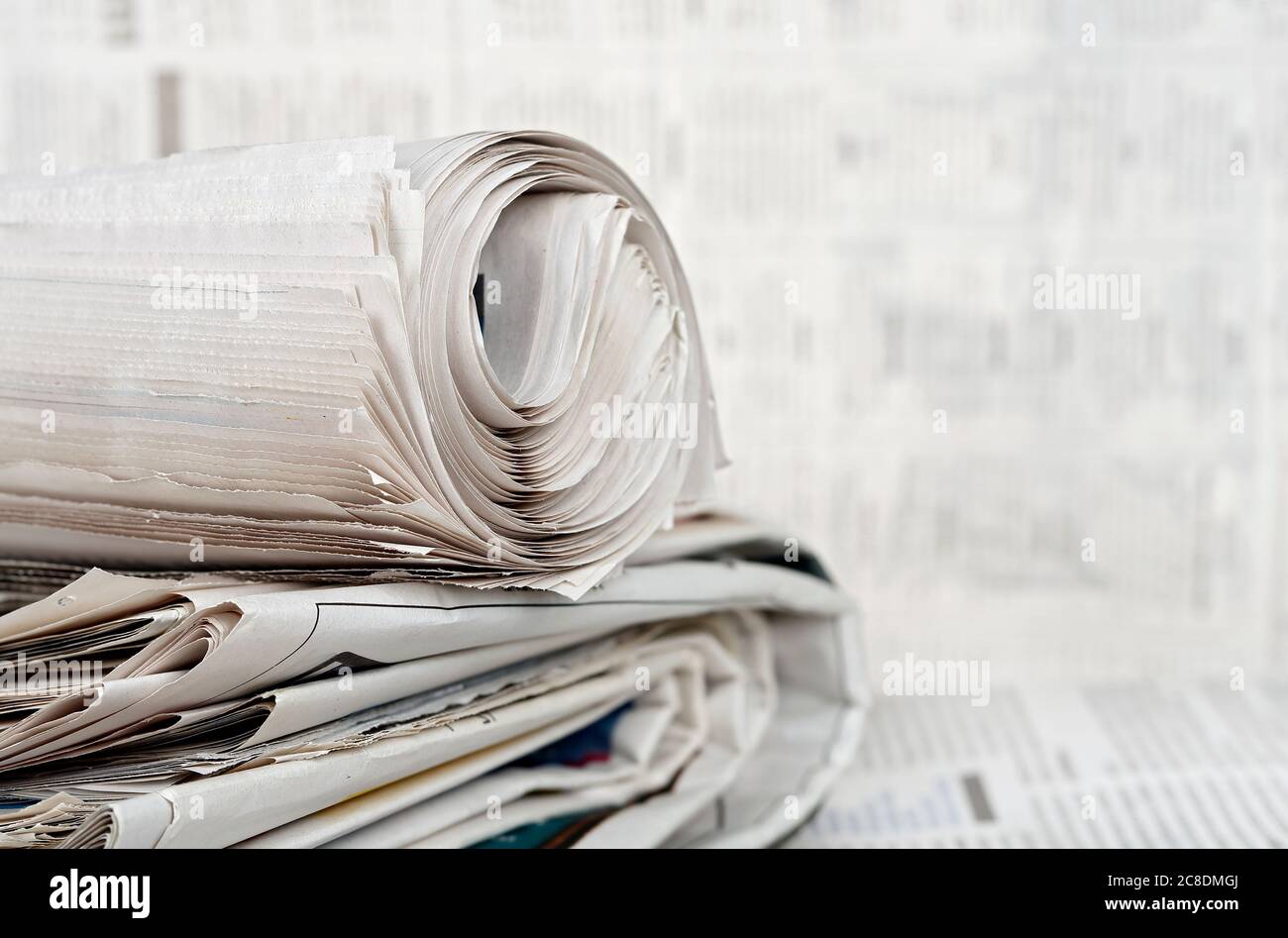giornale rotolato su pila di giornali contro sfondo sfocato Foto Stock