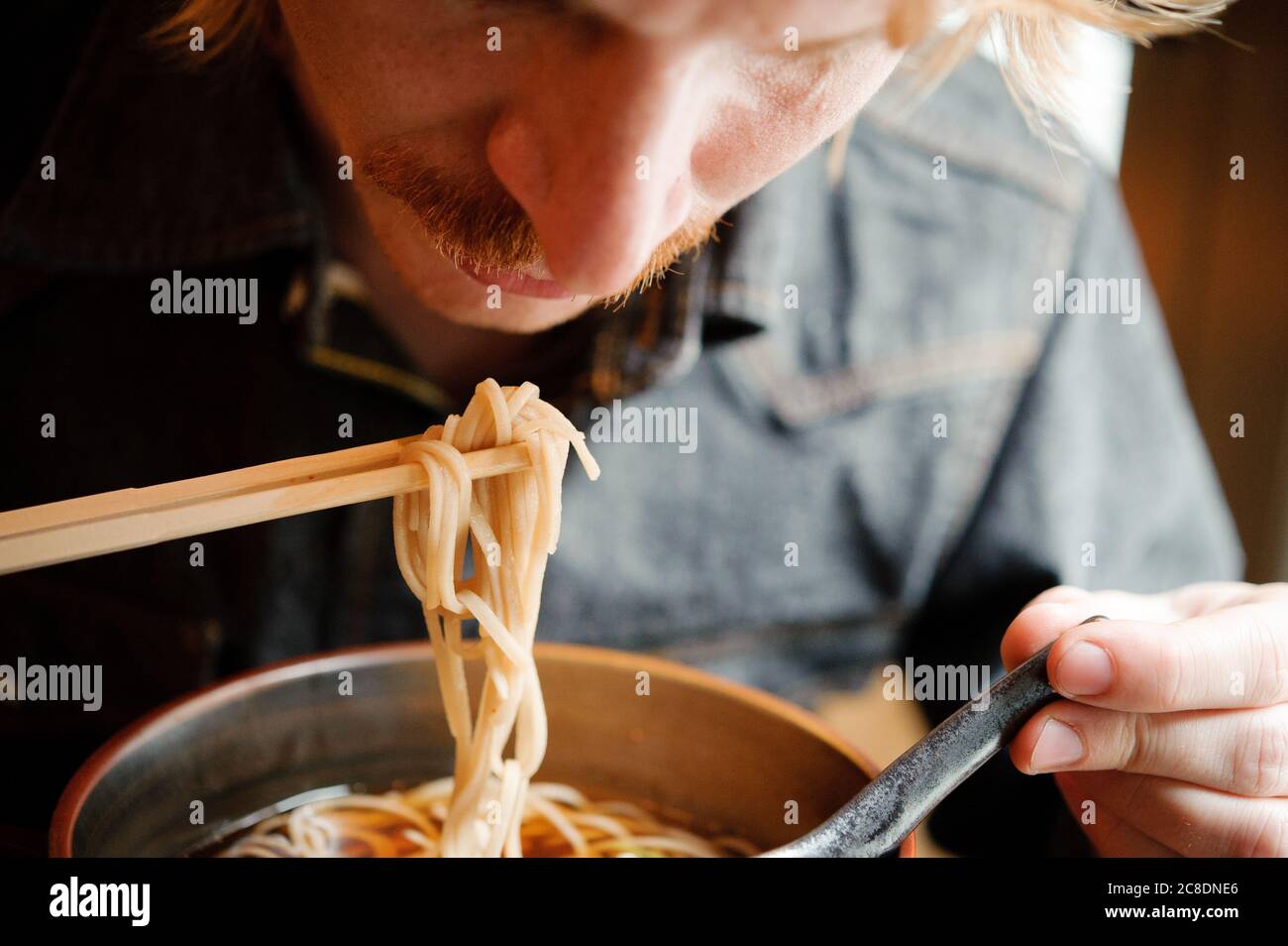 Uomo bianco biondo hipster guardando giù per mangiare e caldo slurp giapponese fibbre noodle soba con chopsticks Foto Stock