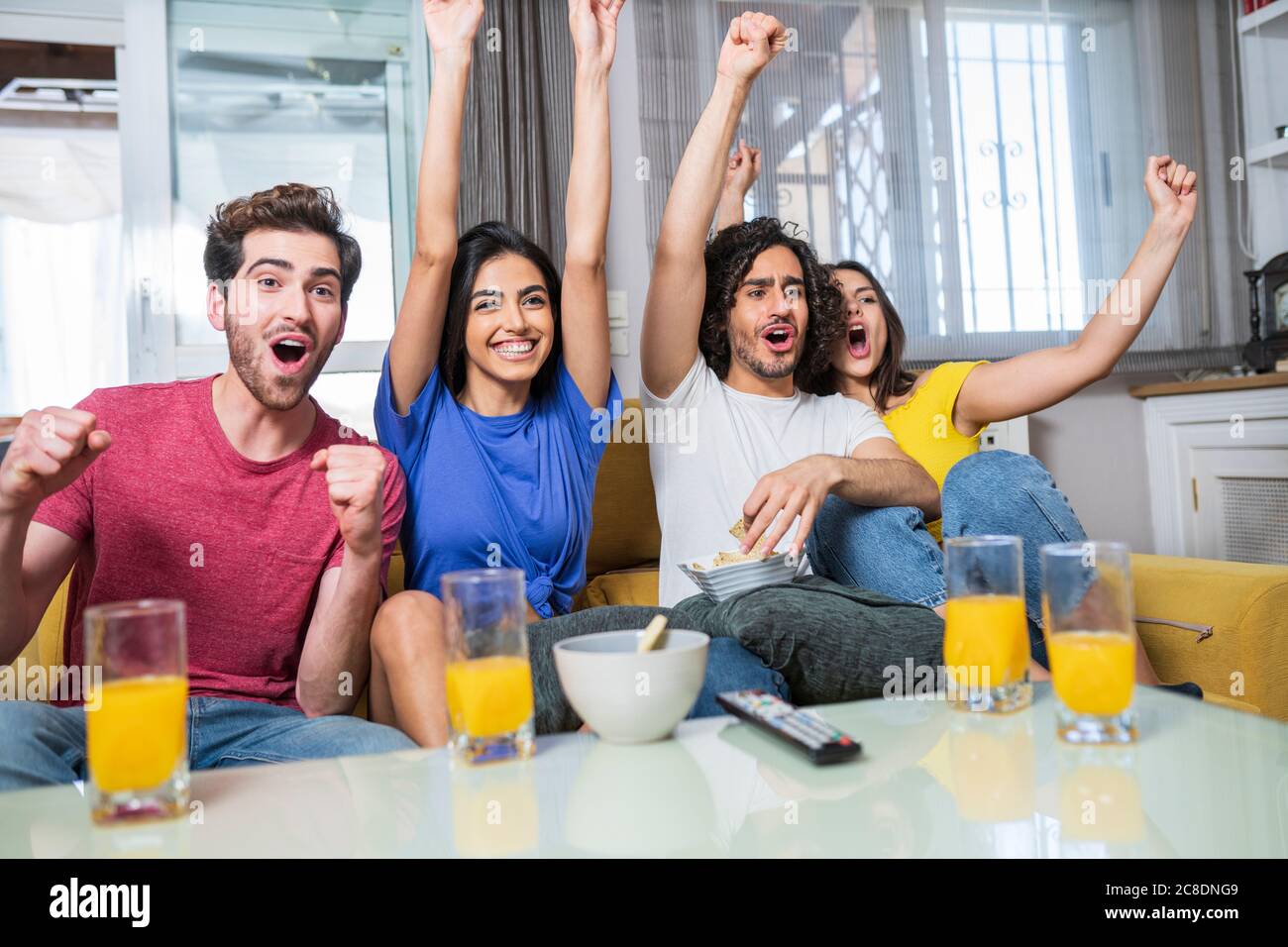 Allegro giovane maschio e femmina tifosi che si acclamano mentre si guarda la TV a casa Foto Stock