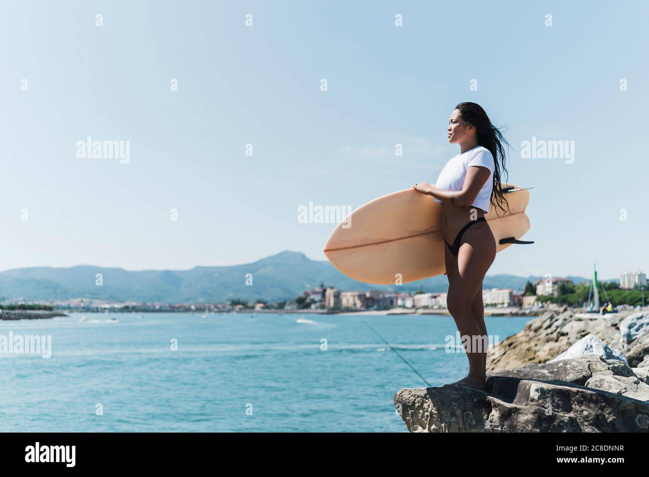 Surfista femminile con tavola da surf in piedi su roccia Foto Stock