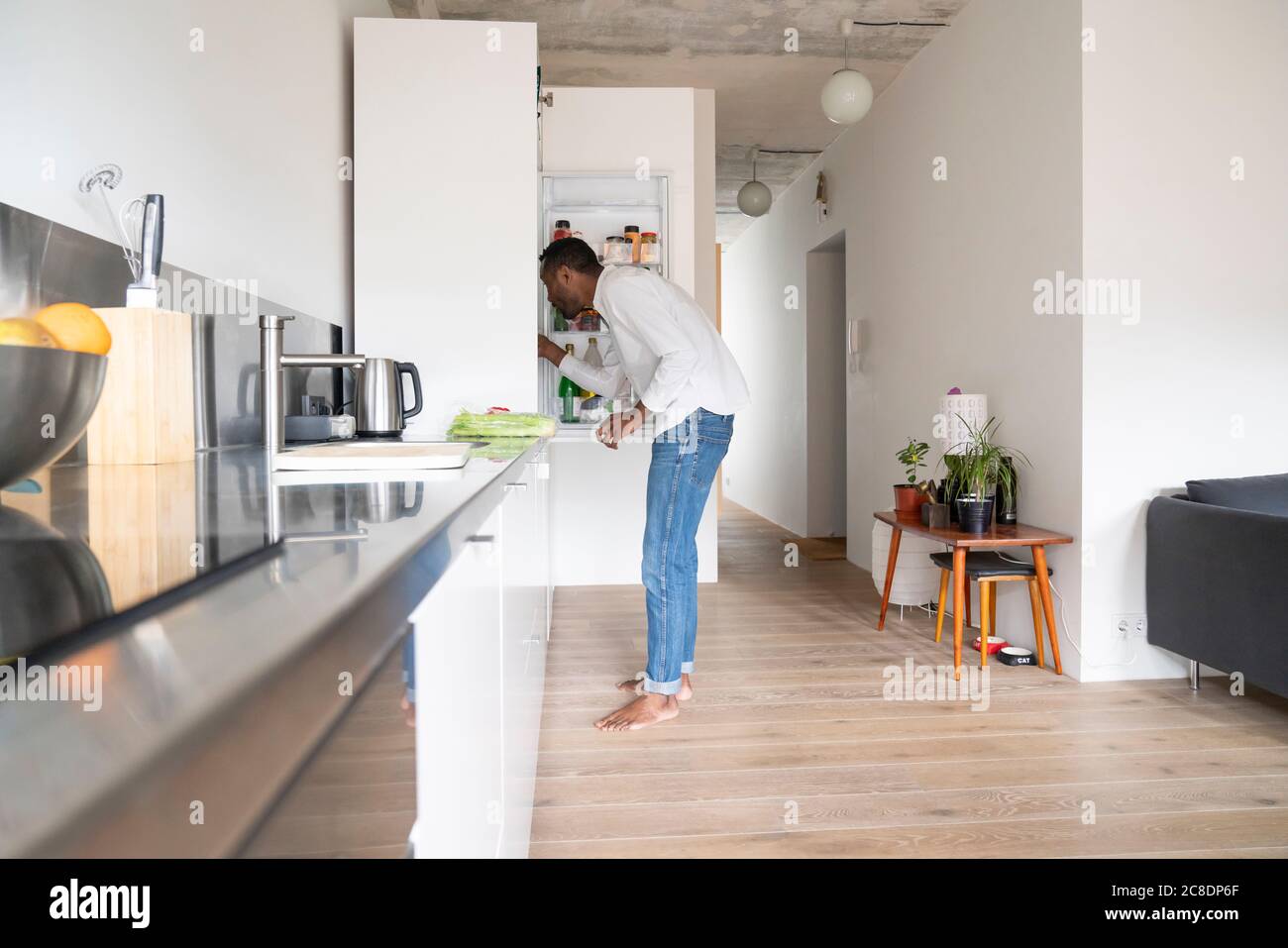 Uomo in piedi in cucina alla ricerca di qualcosa nel frigorifero Foto Stock