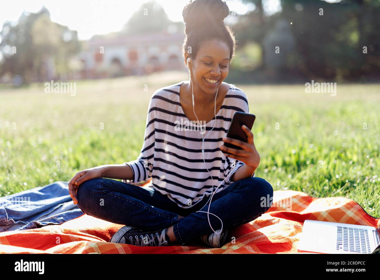 Ritratto di donna sorridente seduto su una coperta l'ascolto della musica con gli auricolari Foto Stock