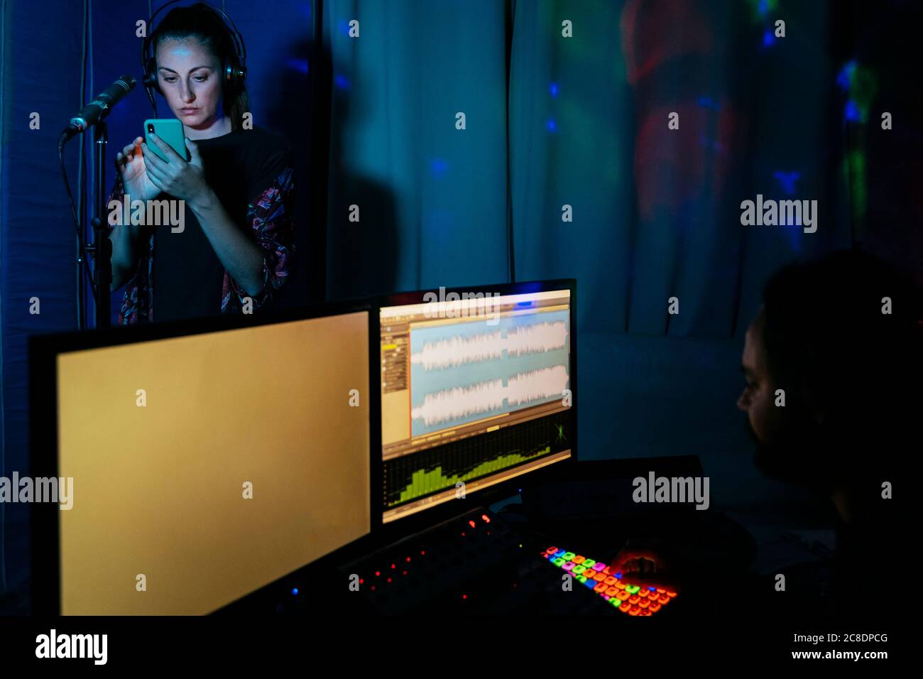 Cantante femminile che usa lo smartphone mentre l'uomo usa il computer studio di registrazione a casa Foto Stock
