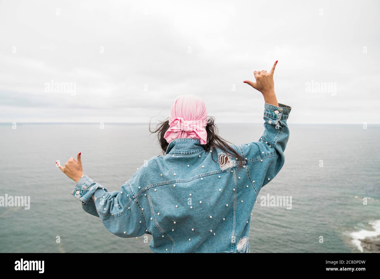 La donna sopravvissuta al cancro gesturing mentre guarda il mare contro nuvoloso cielo Foto Stock