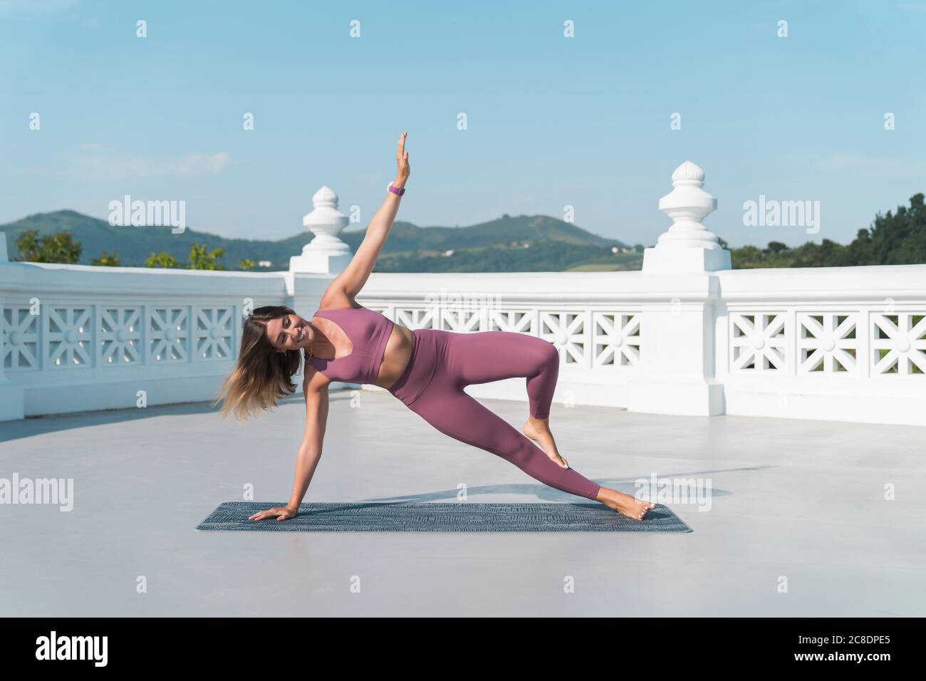 Giovane donna che pratica fianco posare sulla terrazza di costruzione contro cielo Foto Stock
