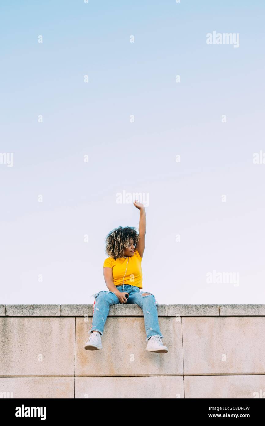 Giovane donna seduta sul muro con braccio rialzato Foto Stock