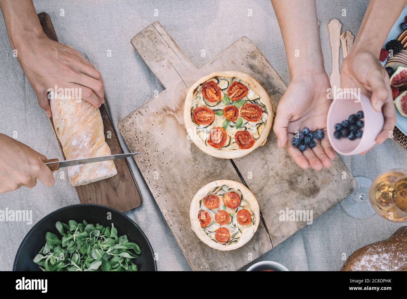 Mani di donna che prendono i mirtilli mentre amico che taglia il pane sopra tabella Foto Stock Mani di donna che prendono i mirtilli mentre amico che taglia il pane sopra tabella Foto Stock