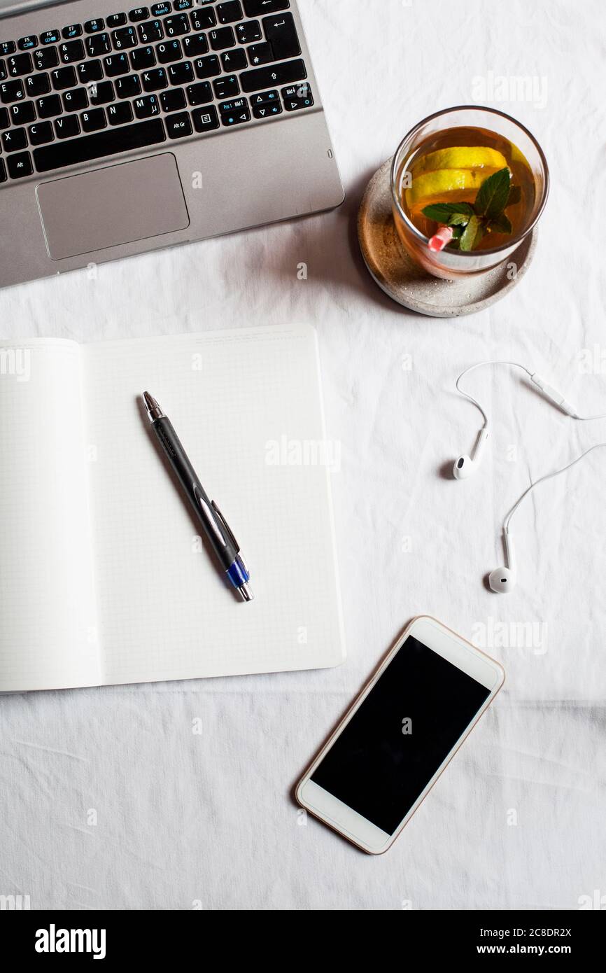 Telefono cellulare con libro e tè da computer portatile sulla scrivania in ufficio Foto Stock