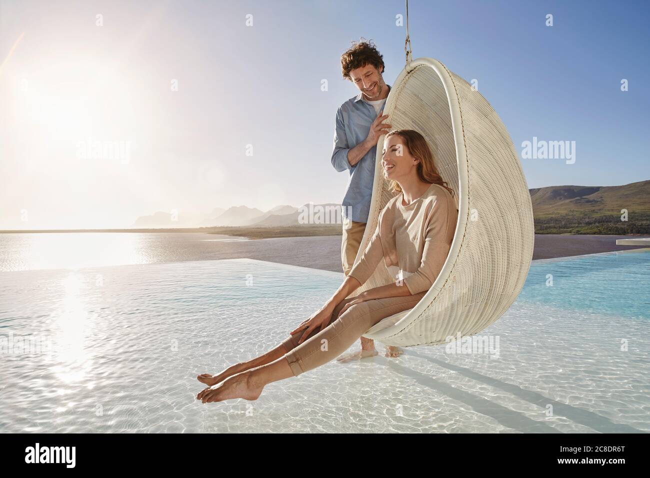 Felice coppia con donna seduta in sedia sospesa sopra nuoto piscina Foto Stock